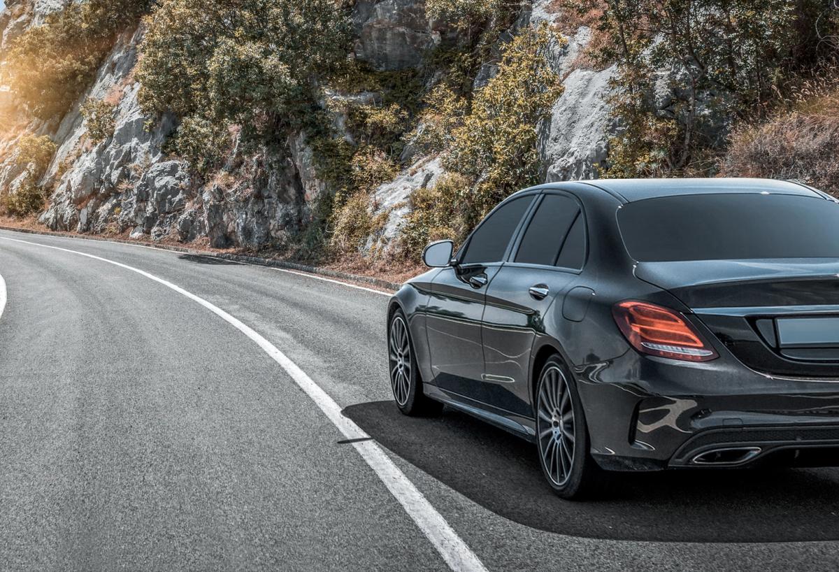 A sleek, black luxury car with a glossy finish reflecting the surroundings. The car features a prominent grille with horizontal slats and the manufacturer’s emblem, modern, illuminated angular headlights, and aerodynamically designed body with smooth lines and curves. The alloy wheels with a multi-spoke design complement the car’s luxurious appearance. This image perfectly represents the high-end vehicles available for luxury rental in Switzerland 