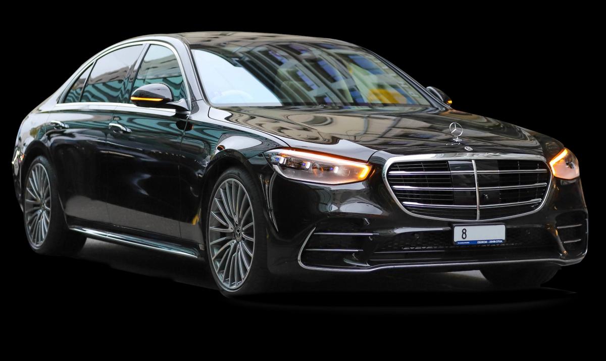 A luxurious, black, glossy-finish car with a prominent grille, manufacturer's emblem, sleek LED headlights, and alloy wheels, reflecting the surrounding lights. Ideal for premium car rental services in Switzerland.