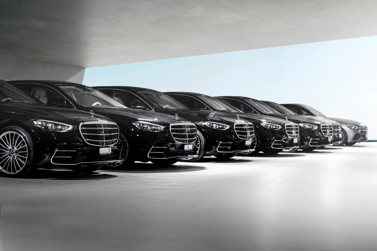 A lineup of luxurious black cars, gleaming under the soft lighting of a modern and minimalist parking area. Each car is identical, showcasing a sleek design with polished surfaces that reflect the soft lighting.